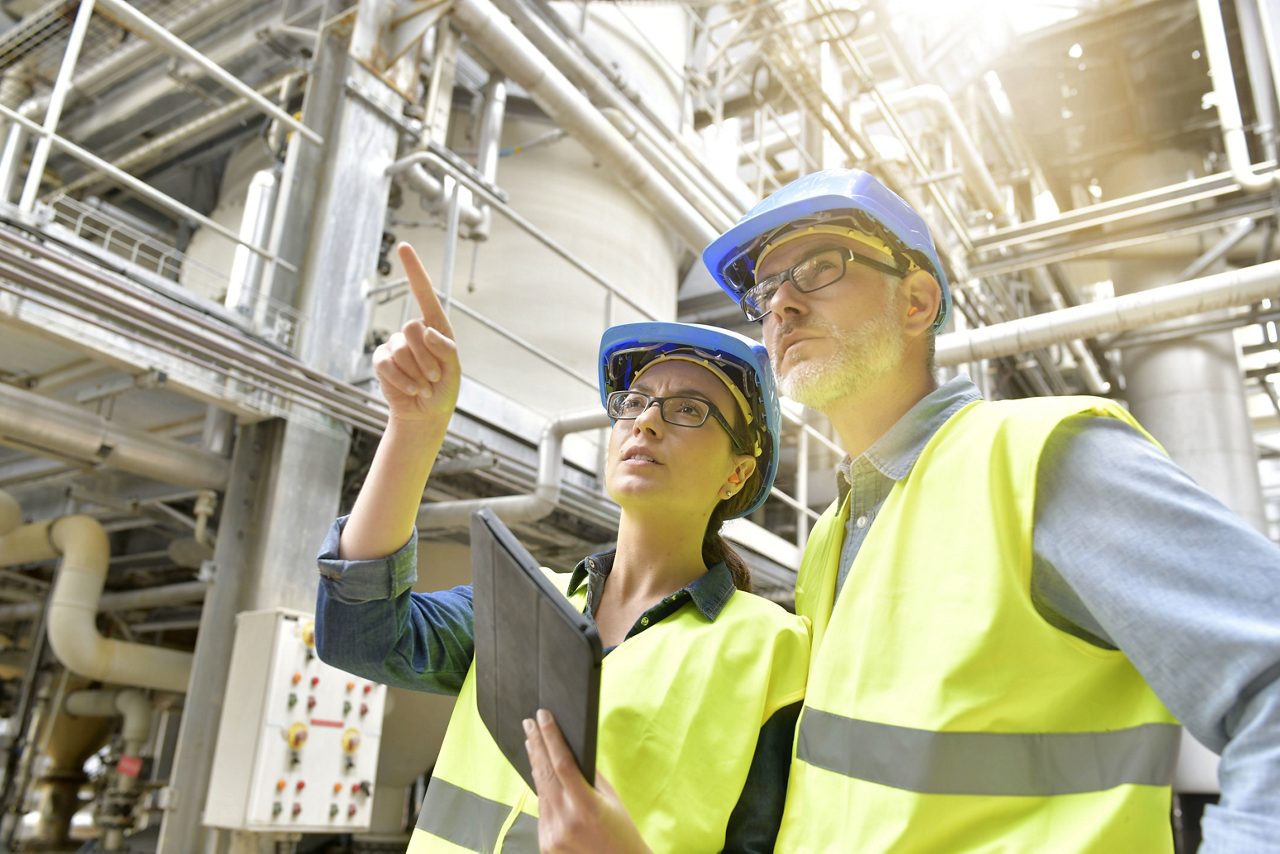 Industrial engineers working in recycling plant with tablet.  Network of pipes in the background.