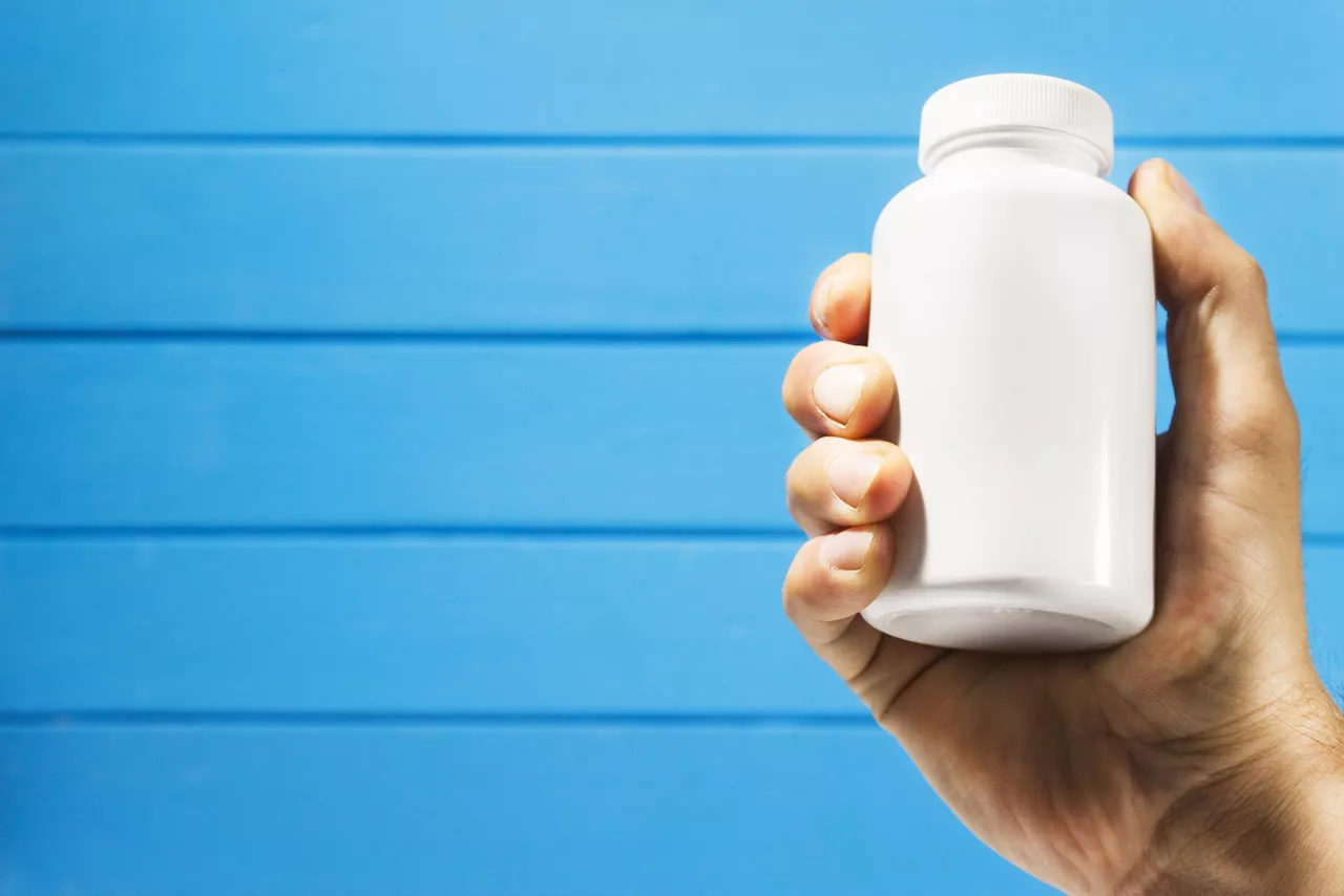 Hand holding up white medicine, pill, or vitamin bottle on slatted blue wall background