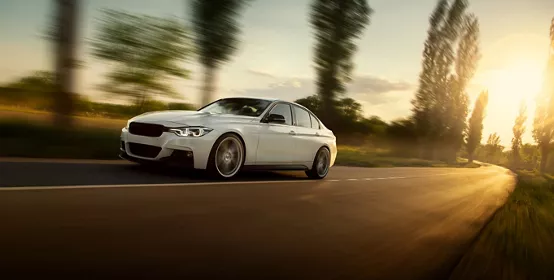 White car is driving on empty countryside asphalt road at sunset