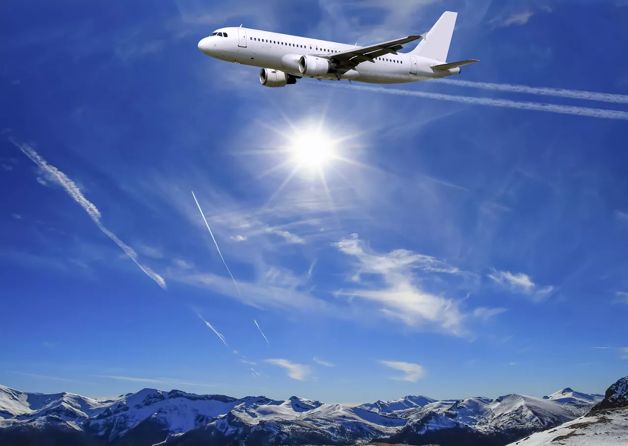 Airplane flying over sunny blue sky and Alpine mountains background