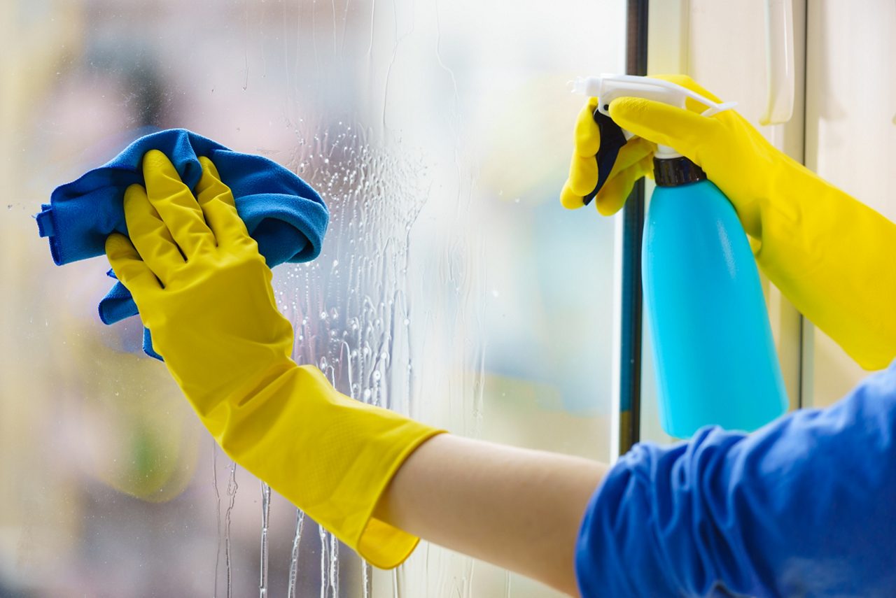 Female hand in yellow gloves cleaning window pane with rag and spray detergent. Cleaning concept