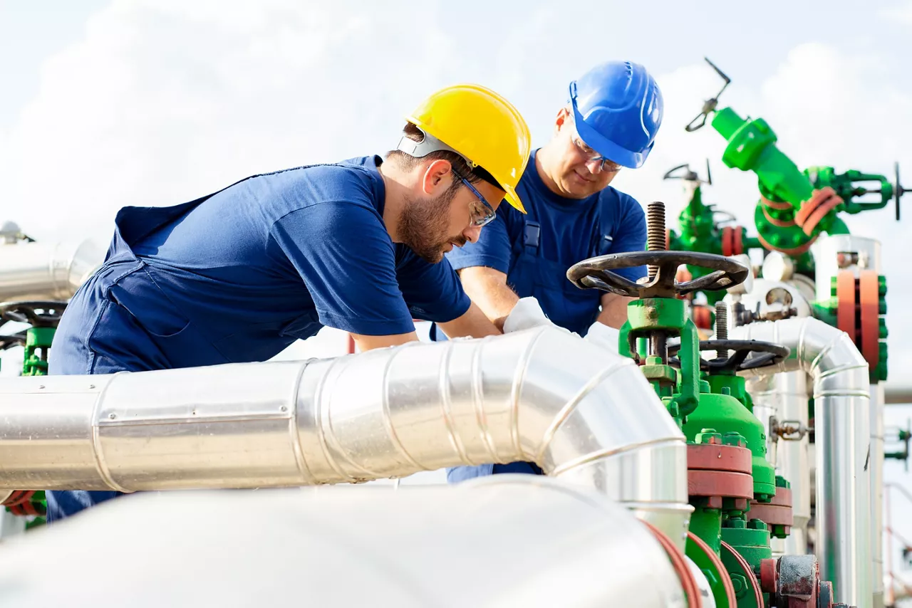 Two petrochemical workers inspecting pressure valves on a fuel tank