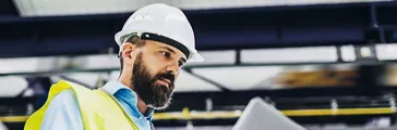 A portrait of a mature industrial man engineer with laptop in a factory, working.