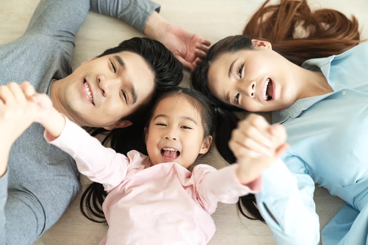 Asian family with holding hands together lying on floor looking at camera