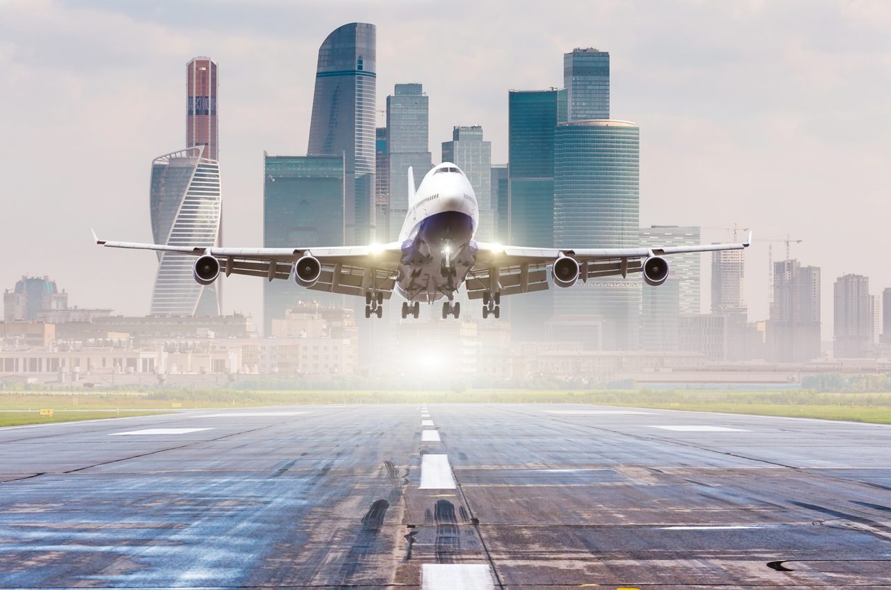 Commercial airplane jetliner approaching for landing on runway, modern city on background