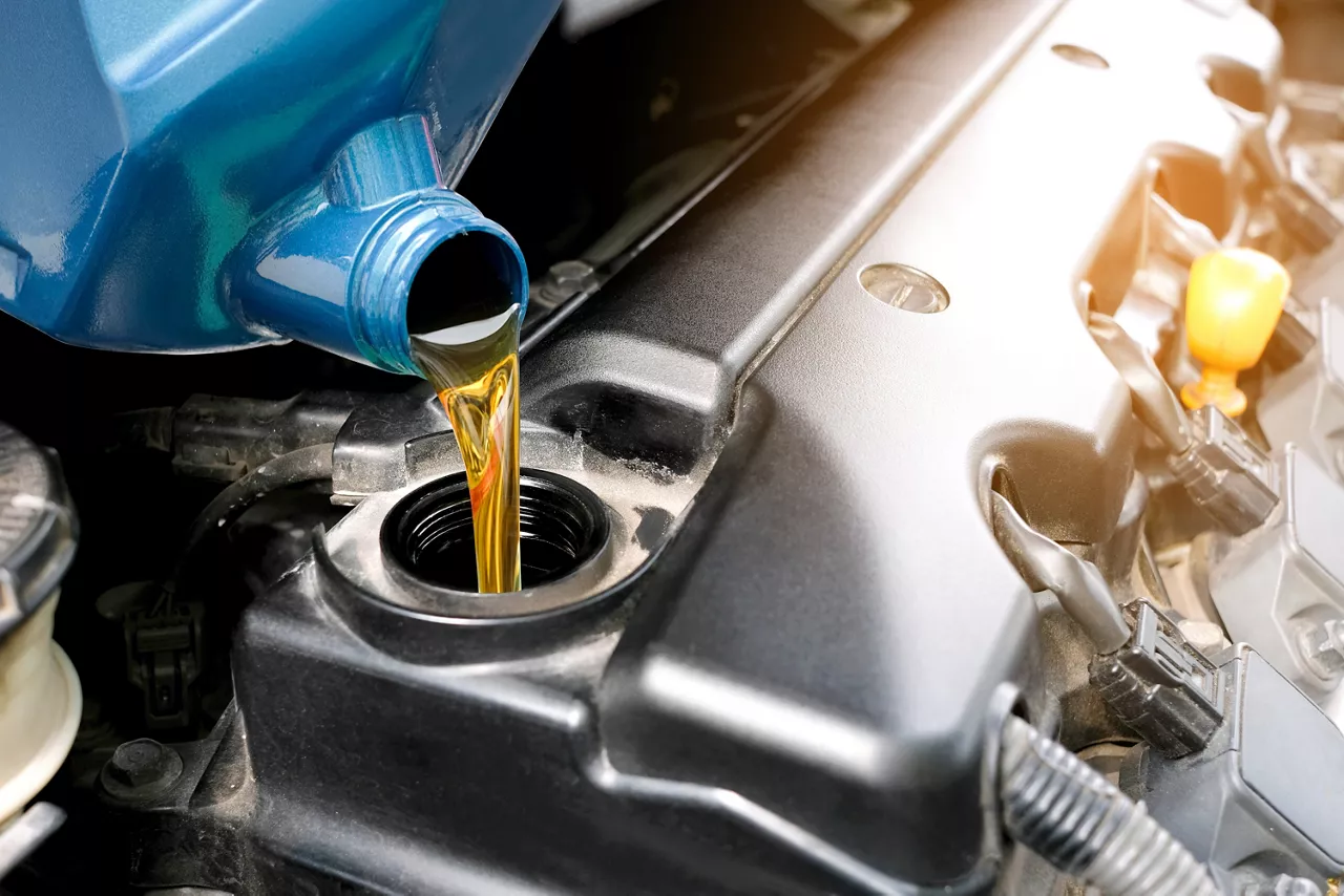 Close up of oil being poured from blue plastic container into black engine