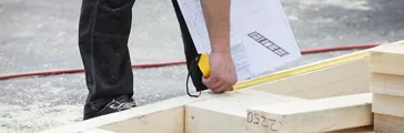 Carpenter measuring wooden 2x4" wall structure, checking the building plan at the building site. Building industry, carpentry concept.