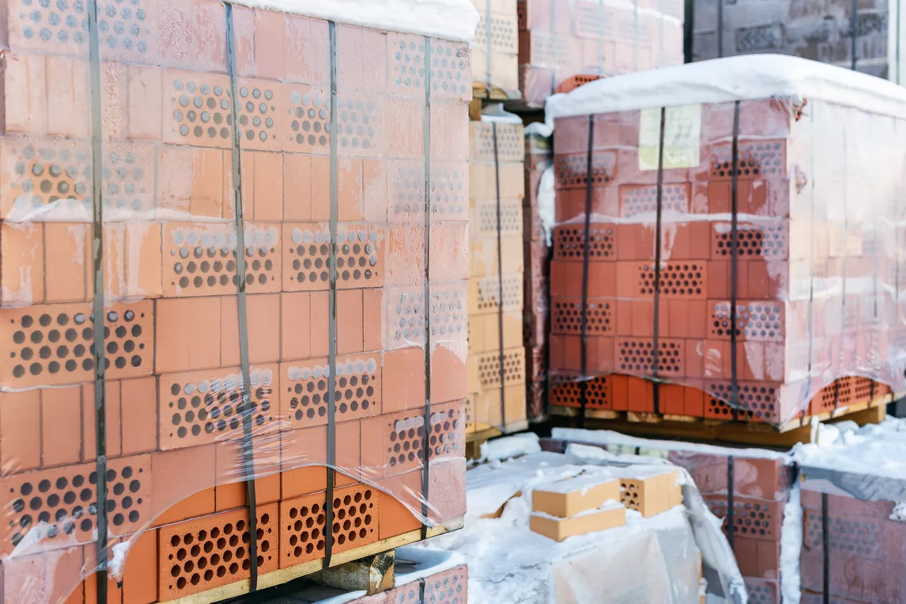 Stock pallets of red bricks wrapped in stretch film at wholesale outdoor market ot store. Construction site with prepared materials.