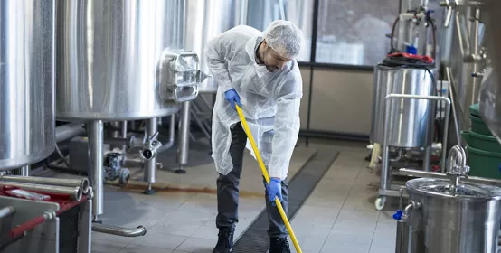 Industrial cleaning service. Professional cleaner wearing protection uniform cleaning floor of production plant.