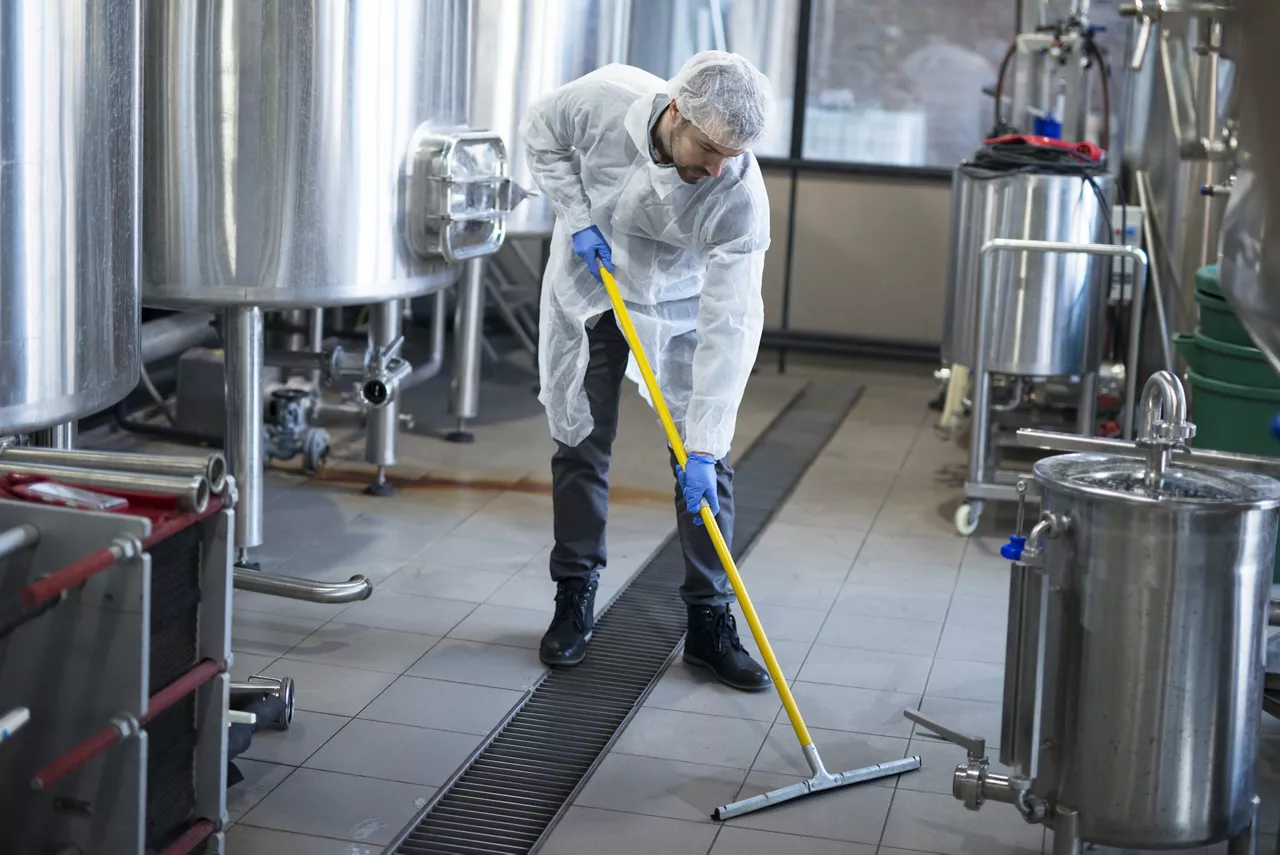 Professional cleaner wearing protection uniform cleaning floor of production plant