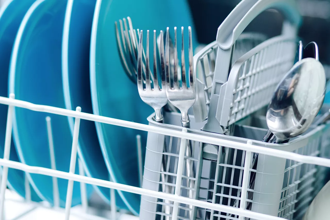 Kitchenware in dishwasher close-up, focus on basket with spoons and forks