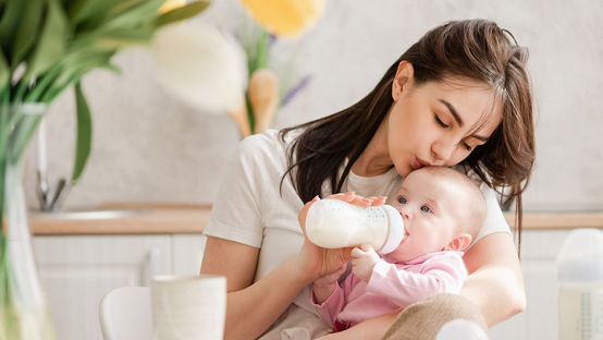 우유를 마시면서 아기에게 입맞춤하는 젊은 어머니 모유 수유. 젖병에 든 분유를 신생아에게 먹이기.