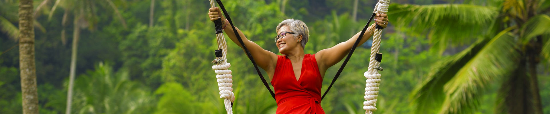 Woman riding rainforest swing in red dress