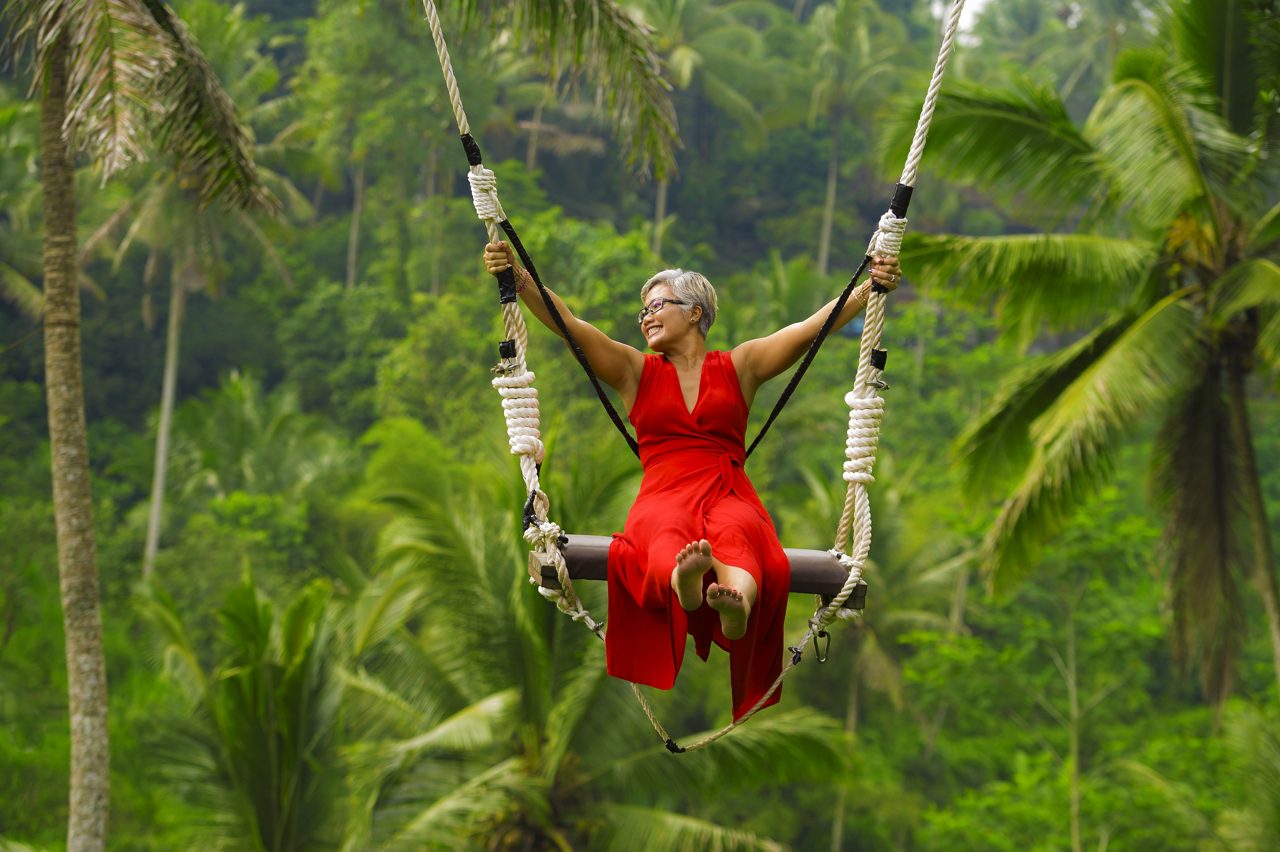 Mulher montando balanço de floresta tropical com vestido vermelho
