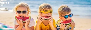 Children eat watermelon on the beach in sunglasses.