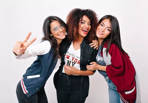 Three women of color smiling and posing with their arms around each other.