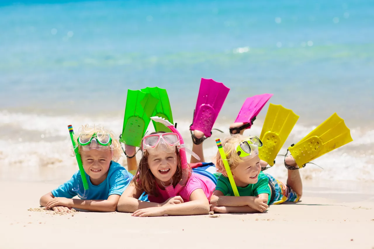 Three children lying on the beach with snorkels and flippers