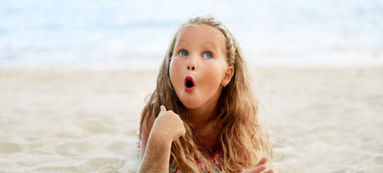 Surprised cute little blonde girl relax on the beach on summer holiday. Funny kids, wow emotions concept