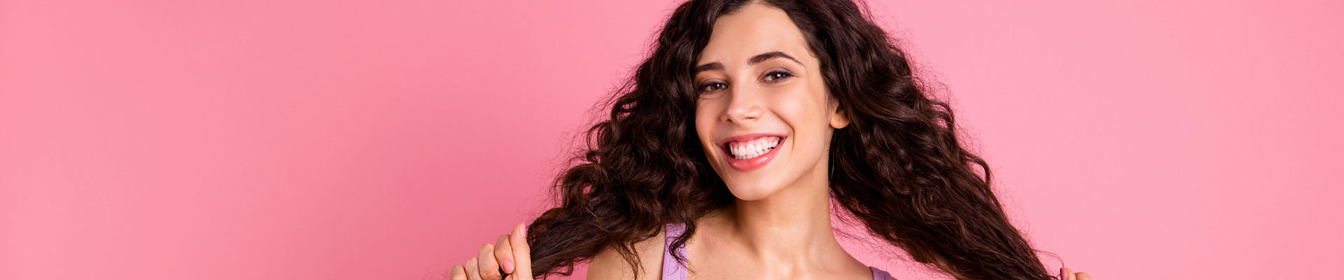 Mulher com cabelos cacheados longos e grande sorriso no fundo branco