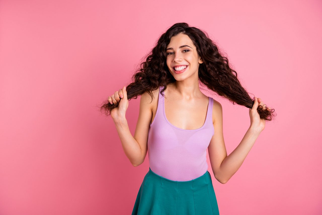 Mulher com cabelos cacheados longos e grande sorriso no fundo branco