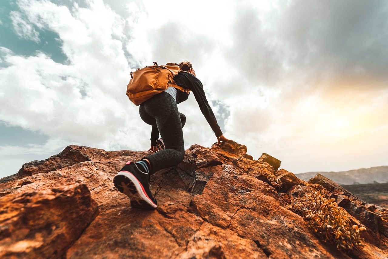 Mujer joven con una mochila trepando a la cima de la montaña