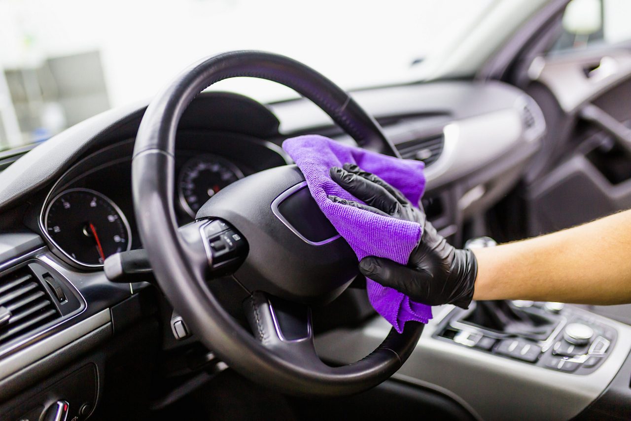 紫色の布を使って車の内装を掃除する手のクローズアップ