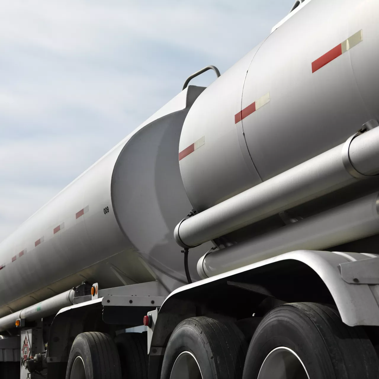 Wheels and tank of a fuel tanker with a background of a cloudy sky.