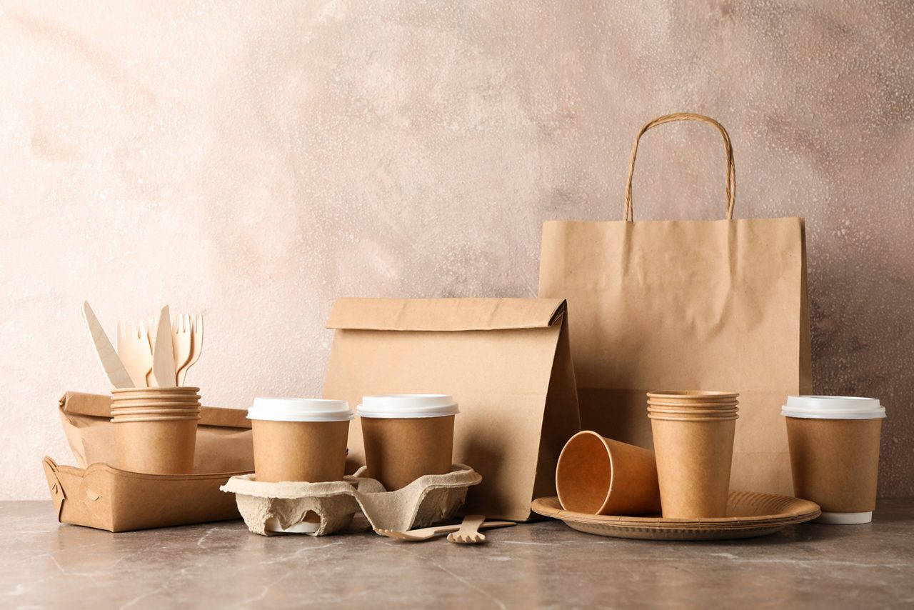 Eco - friendly tableware and paper bag on grey table, space for text