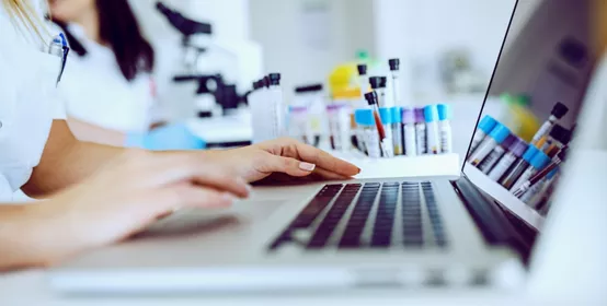  Close up of female lab assistant in white uniform sitting in lab and using laptop 