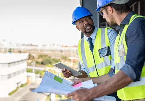 Construction workers talking about new construction site with copy space. Engineers in mechanical factory reading instructions. Architect in construction uniform holding blueprint and discussing.