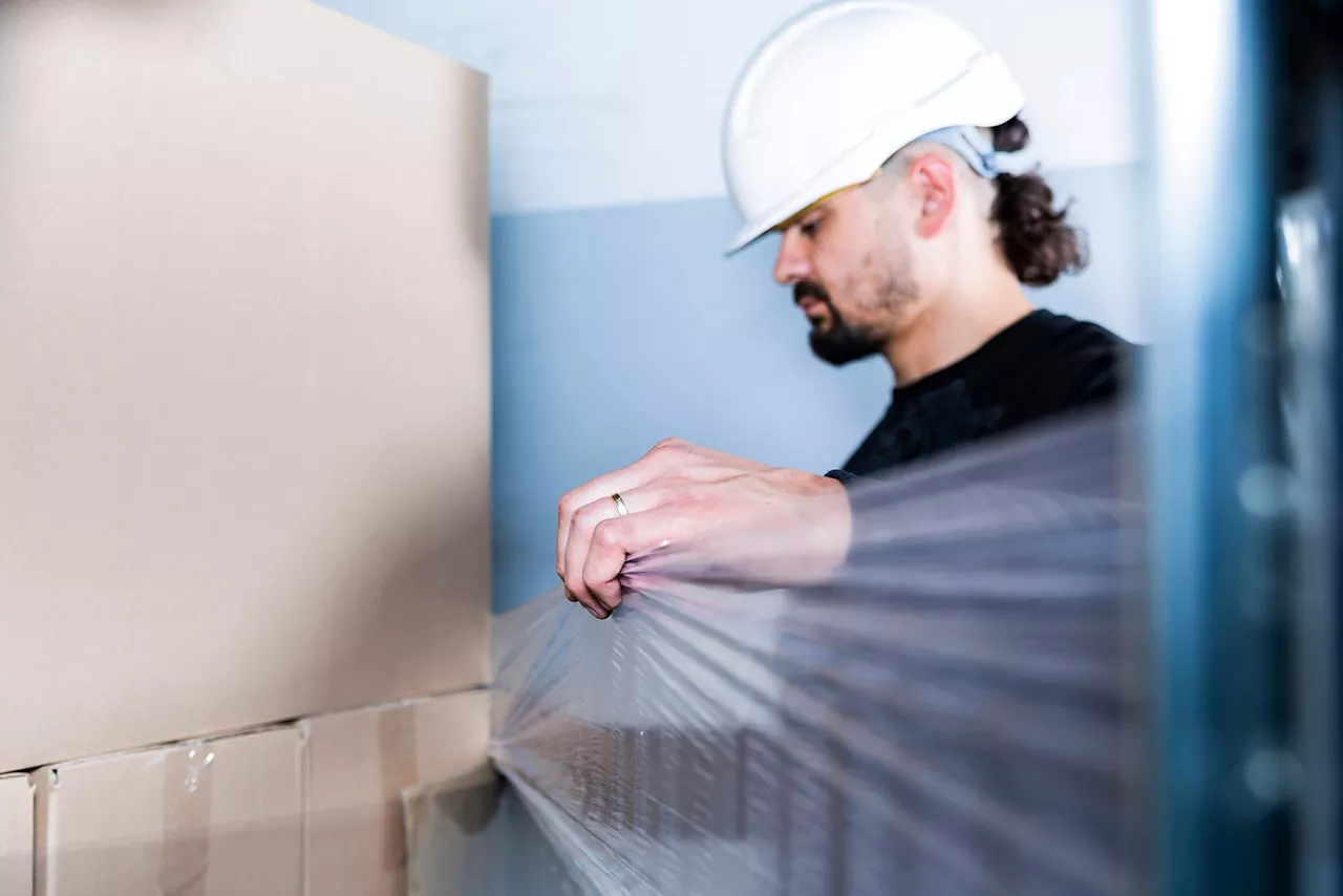 Man secures manufactured goods in carton boxes with stretch wrap