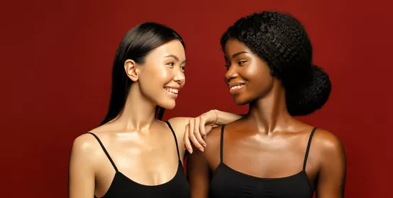 African and Asian women posing and smiling against red background.