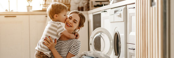 Madre con un hijo frente a una cesta de lavandería llena de ropa blanca