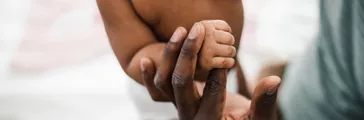 Close up of baby girl tiny hand holding father finger stock photo