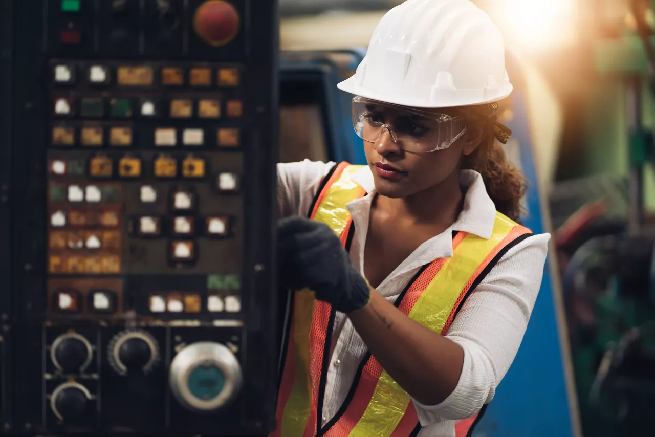 Female worker with safety helmet and safety goggles checking equipment in a factory