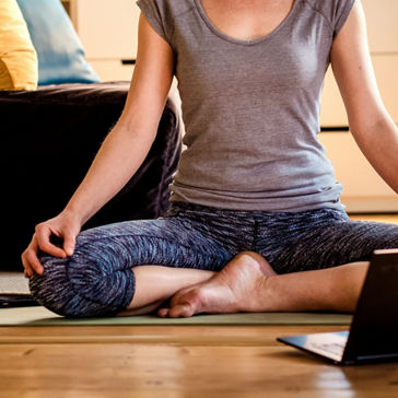 mulher fazendo ioga no piso de madeira enquanto assiste a vídeos no laptop