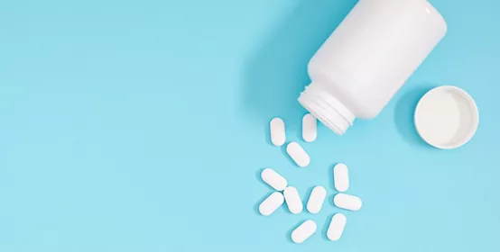 White pills spilled out of white bottle on light blue background