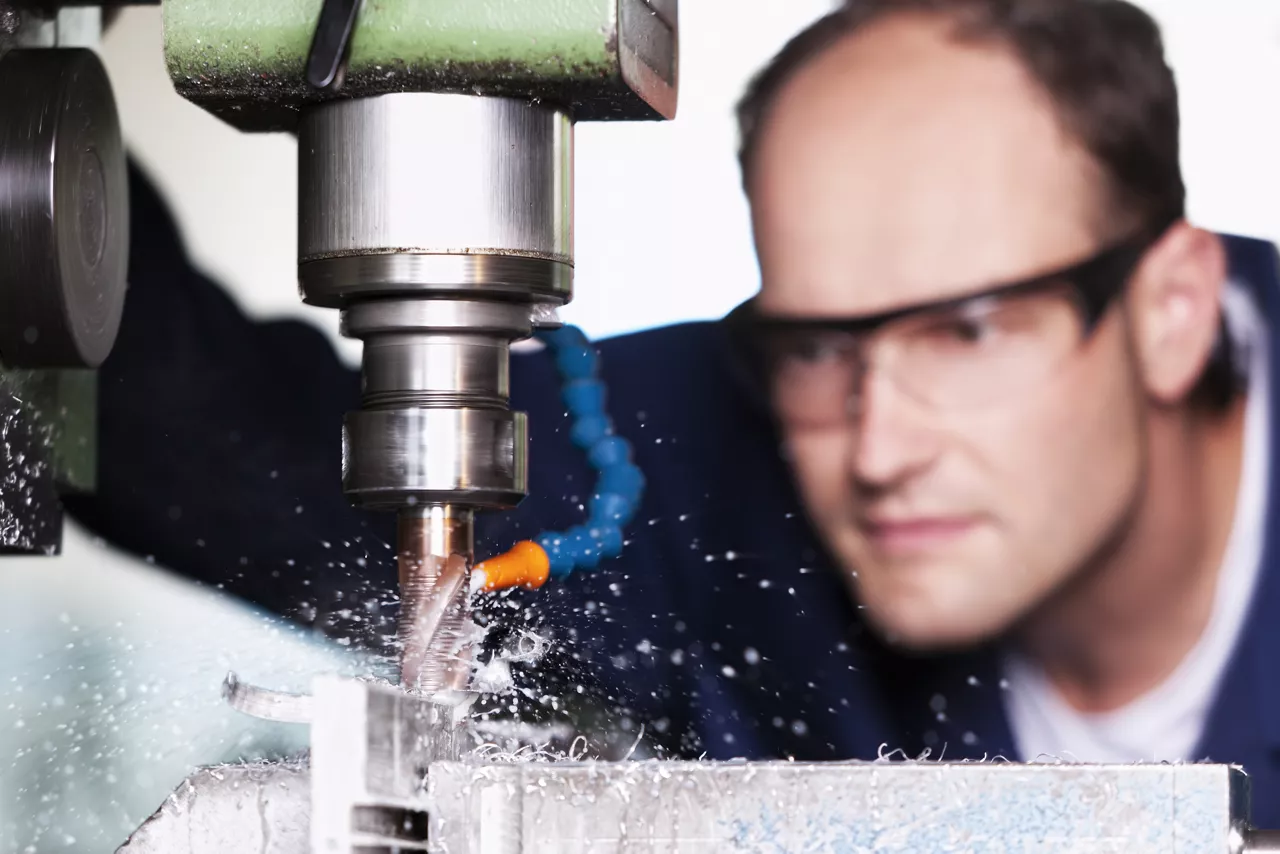 Close up of worker with safety glasses at milling machine in workshop.