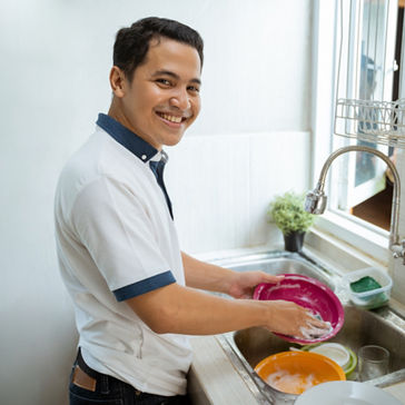 Jovem asiático feliz com camisa branca em pé e lavando pratos na cozinha