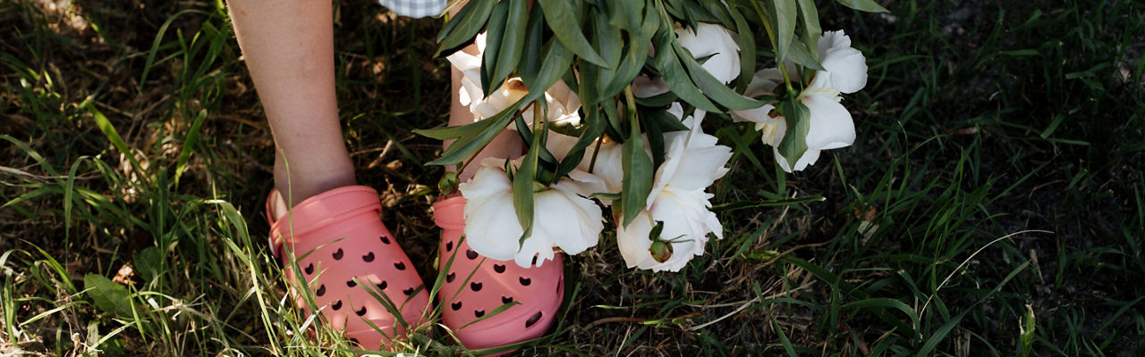 A child holds a bouquet of peonies with buds down.