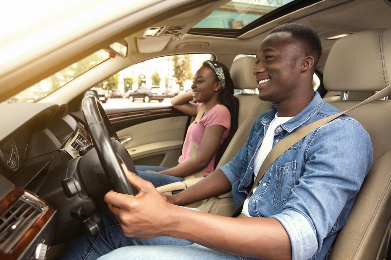 Cheerful African American young couple in car, side view.