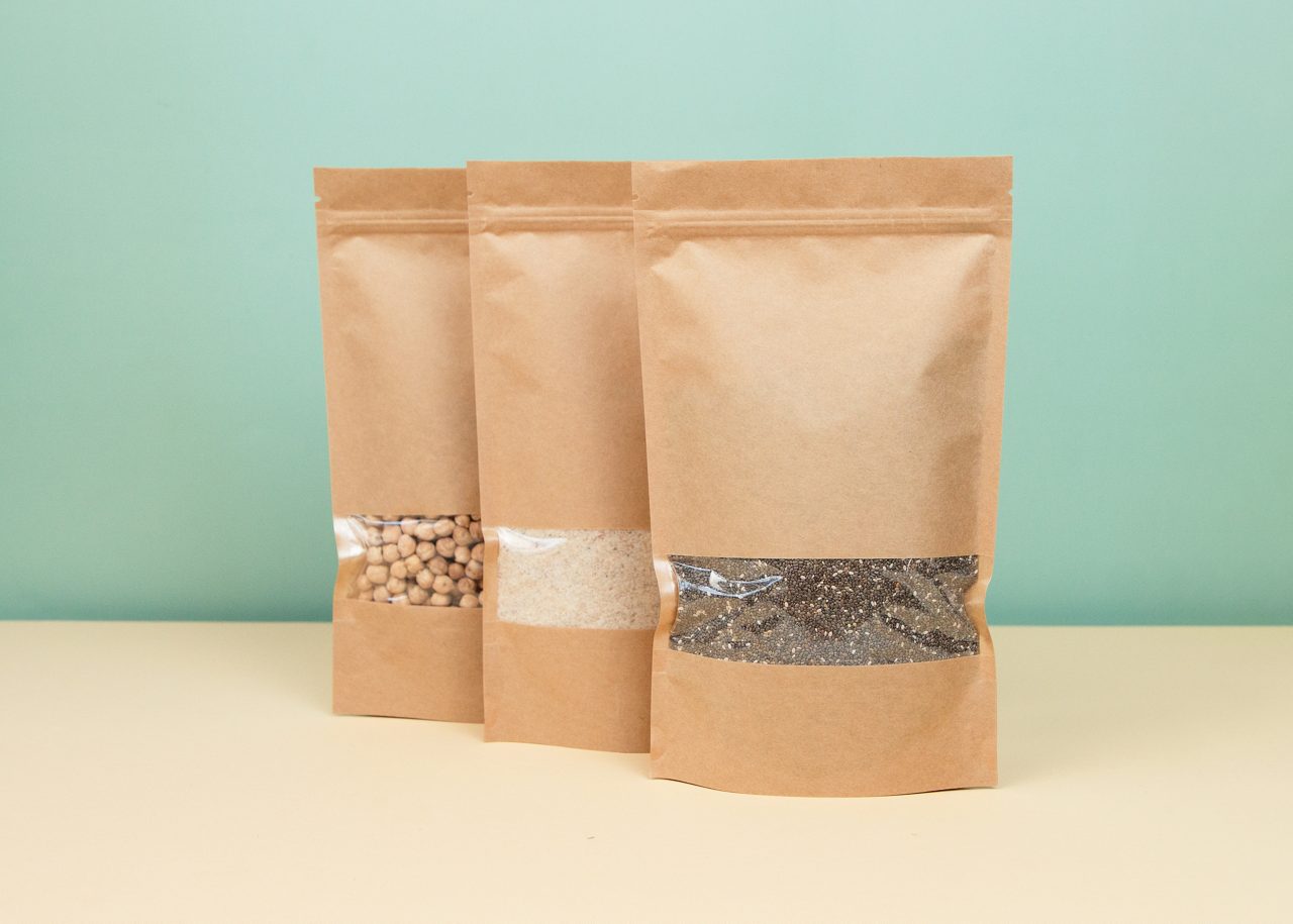 Brown kraft paper doypack bags with groceries front view on a yellow background. Packaging for foods and goods template mock-up. Packs with windows for weight products. Trendy color