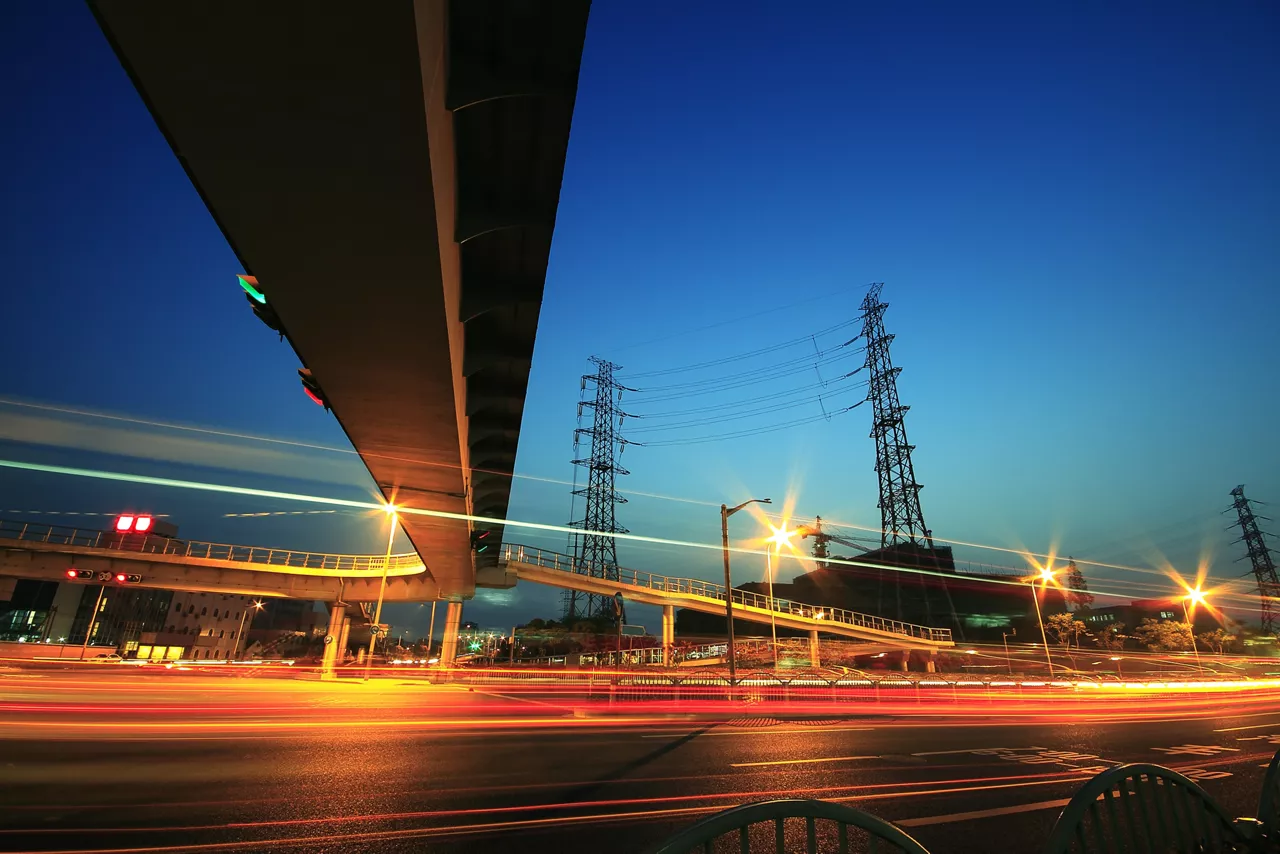 Long exposure of cars passing through city-highway and transmission tower  