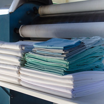 Lençóis brancos, verdes e azuis recém-lavados e dobrados na lavanderia institucional 