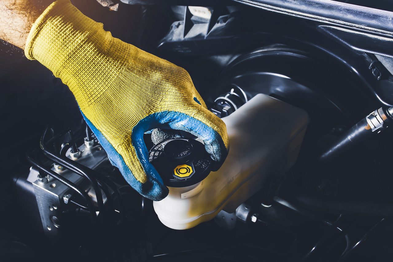 The mechanic is open or close the car's brake fluid reservoir cap to check the brake fluid level.