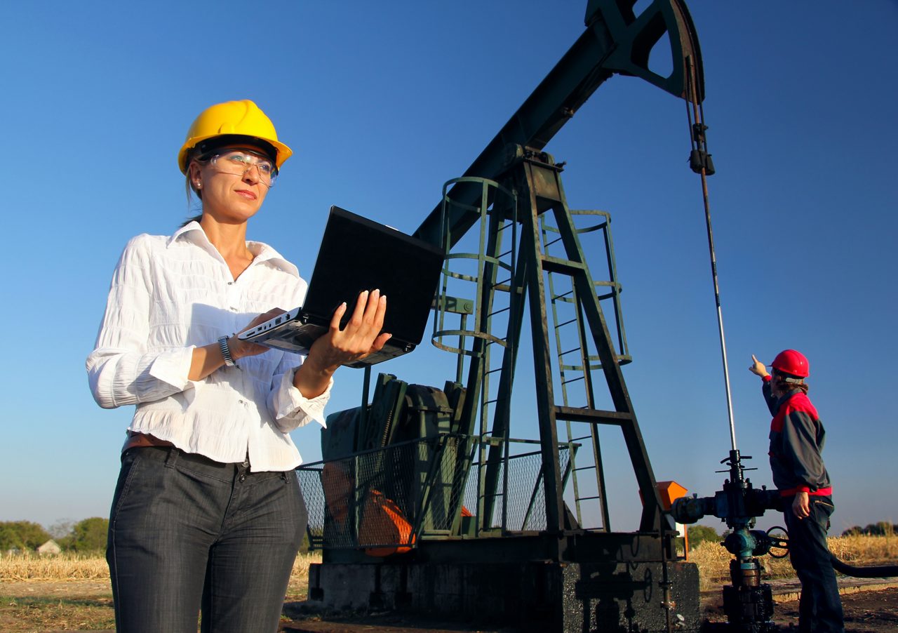 Funcionário em pé no campo petrolífero com laptop