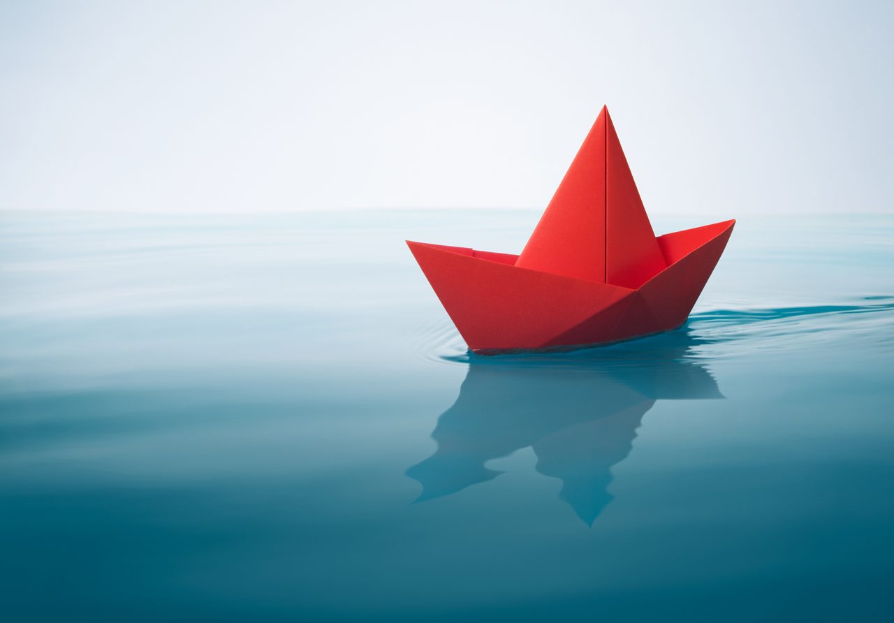 red paper boat sailing on water with waves and ripples