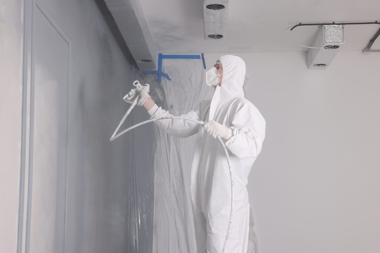 Decorator dyeing wall in grey color with spray paint indoors.