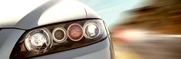A car driving on a motorway at high speeds, overtaking other cars. Close-up on headlight of the car with motion blur in the background.