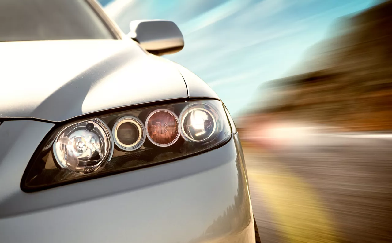 A car driving on a motorway at high speeds, overtaking other cars. Close-up on headlight of the car with motion blur in the background.